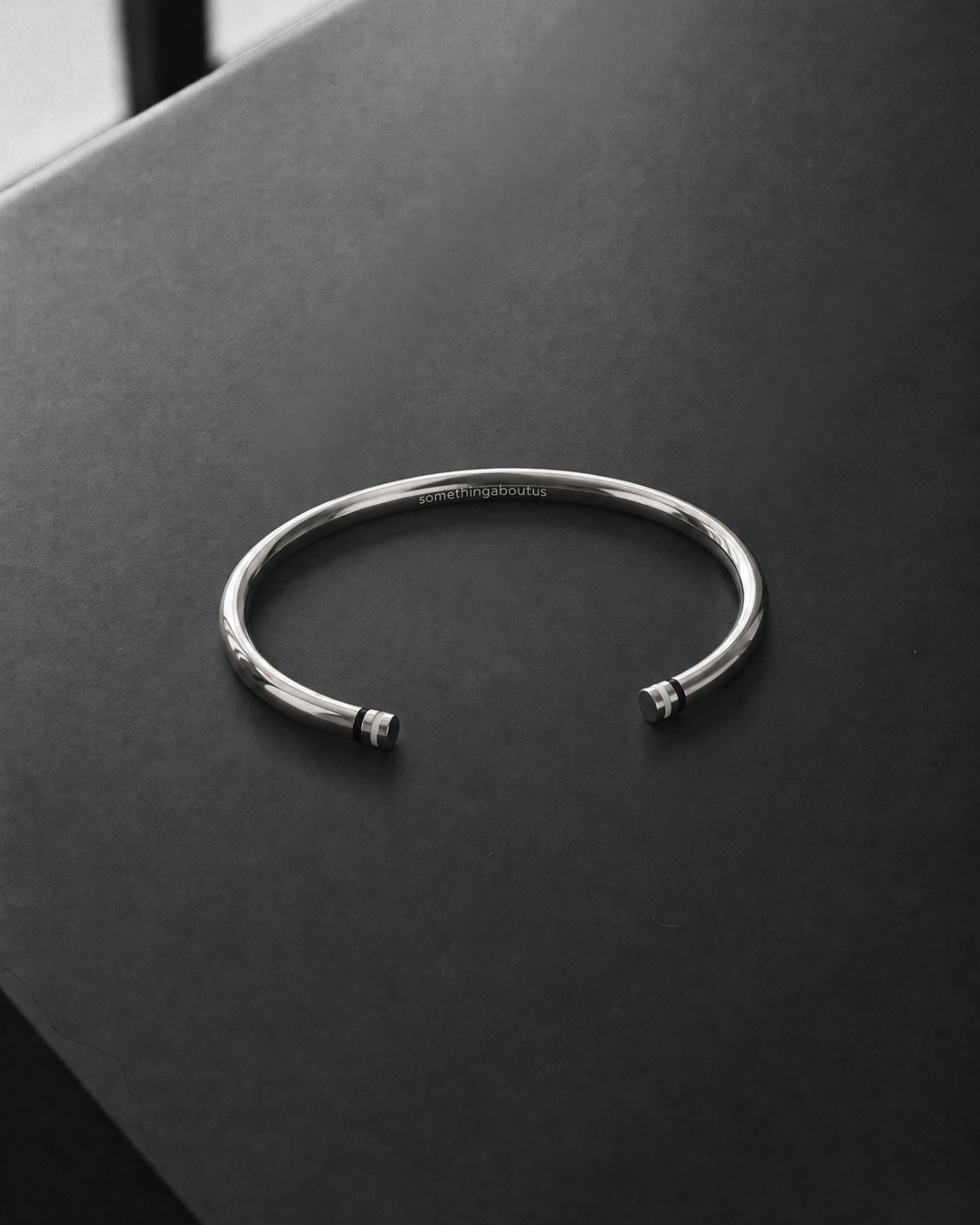 A polished silver cuff bangle bracelet with small bead details at the open ends, resting on a dark gray textured surface.