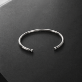 A polished silver cuff bangle bracelet with small bead details at the open ends, resting on a dark gray textured surface.
