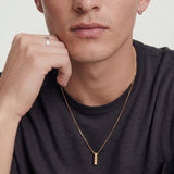 Man wearing a gold necklace with a minimalistic pendant on a plain background