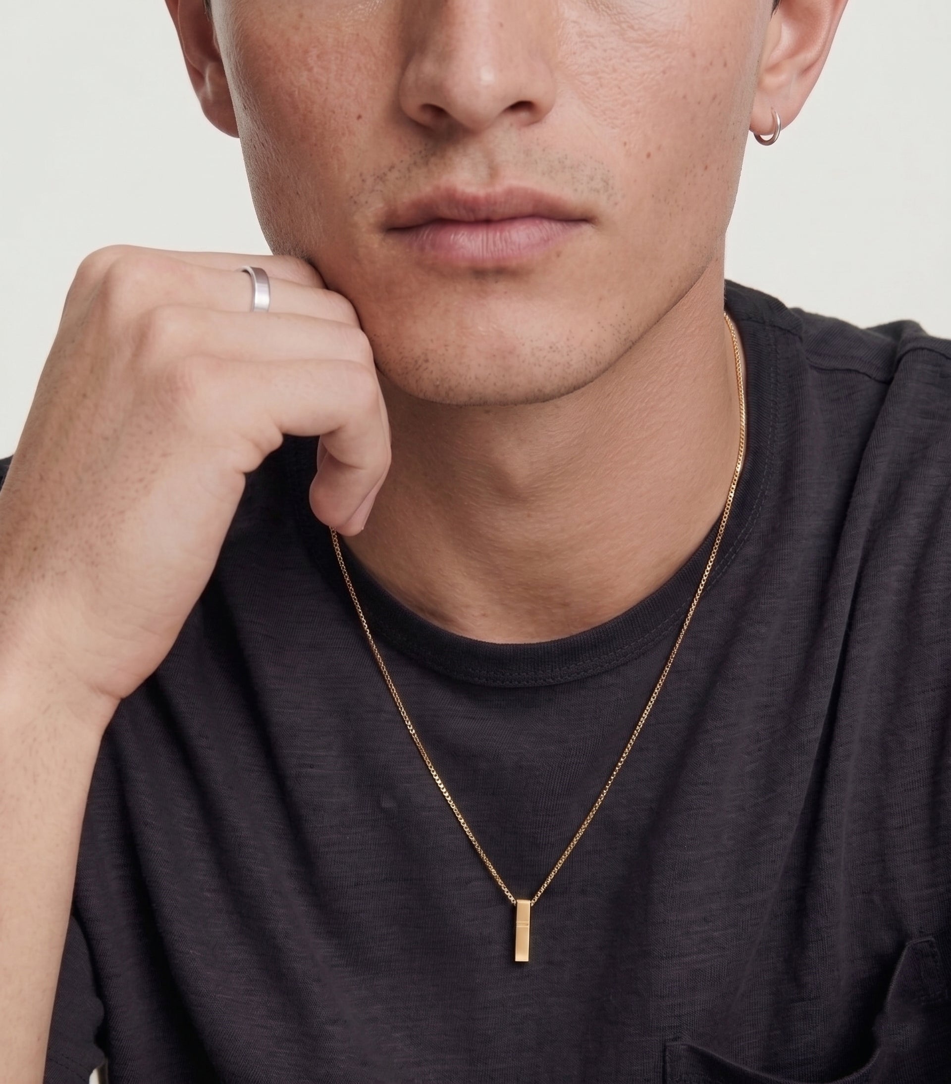 Man wearing a gold necklace with a minimalistic pendant on a plain background